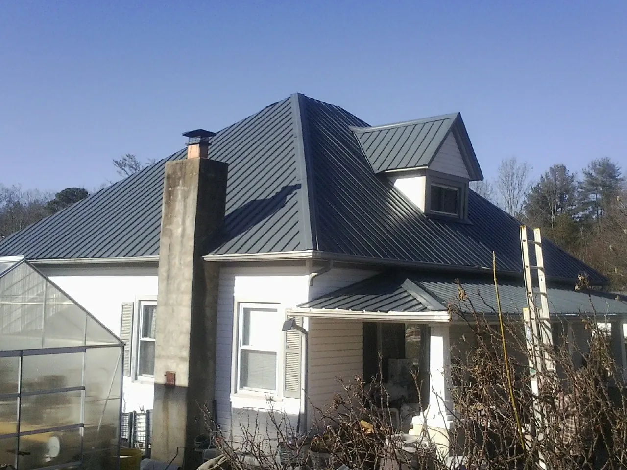 Dark blue standing seam metal roof on a white farmhouse with dormer — Slate & Tile Roof Repair by Roofing Brothers in Montoursville