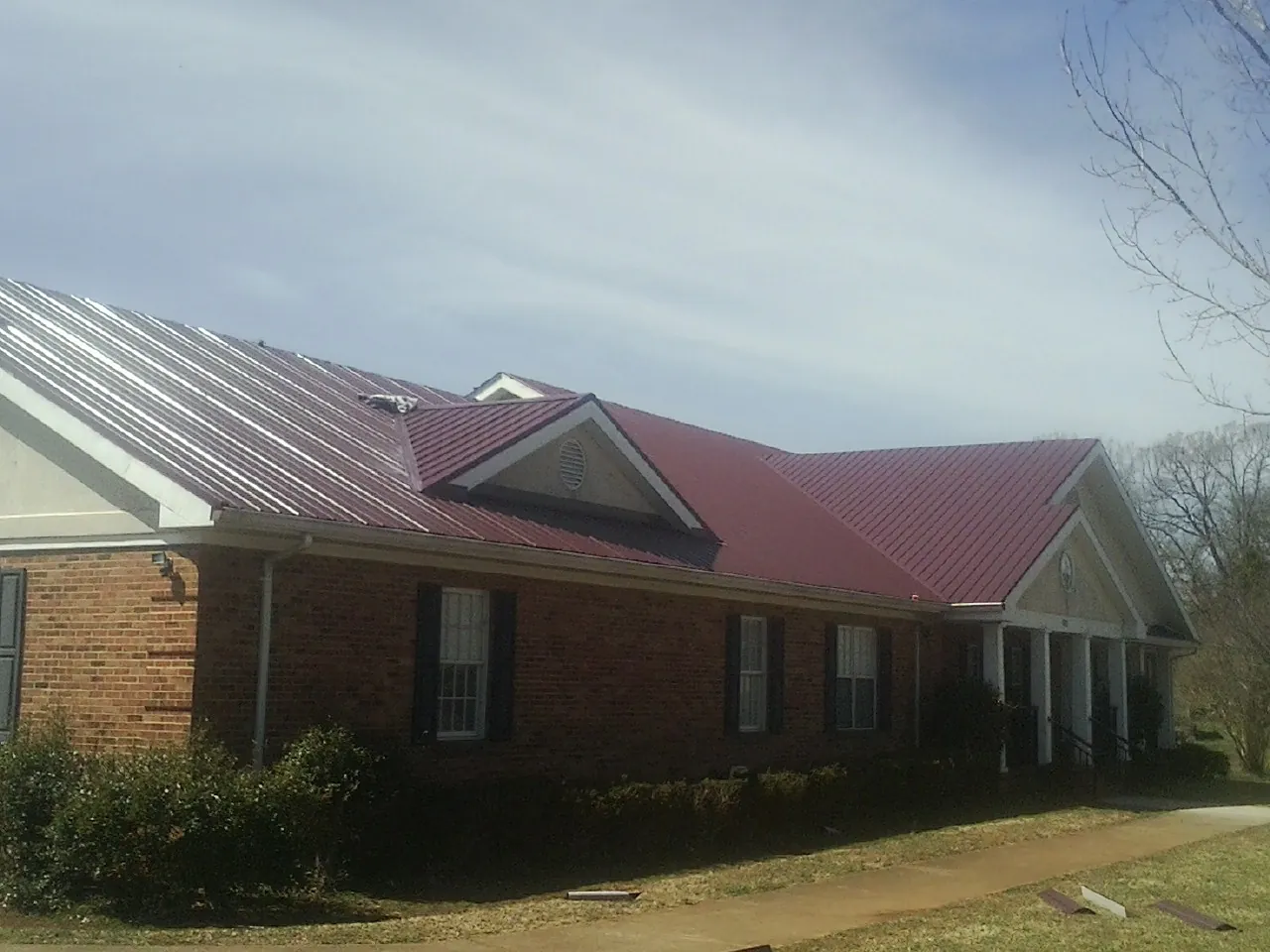 Red metal roof with gabled entries on a long brick building, from a Hail Damage Roof Repair job in Montoursville