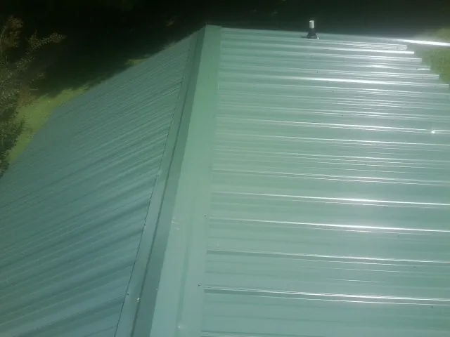 New green metal panels meeting at the ridge of a roof — Flat Roof Repair work by our crew in Montoursville