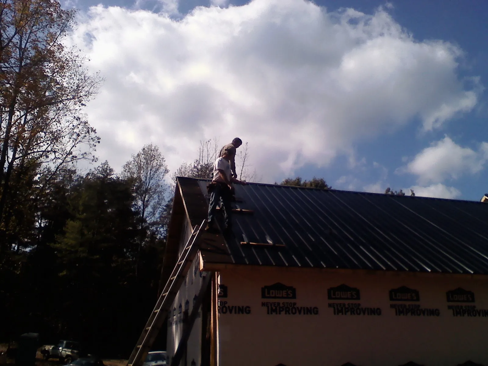 Roofer fastening dark metal panels high against a cloudy sky, from a Roof Inspection job in Montoursville