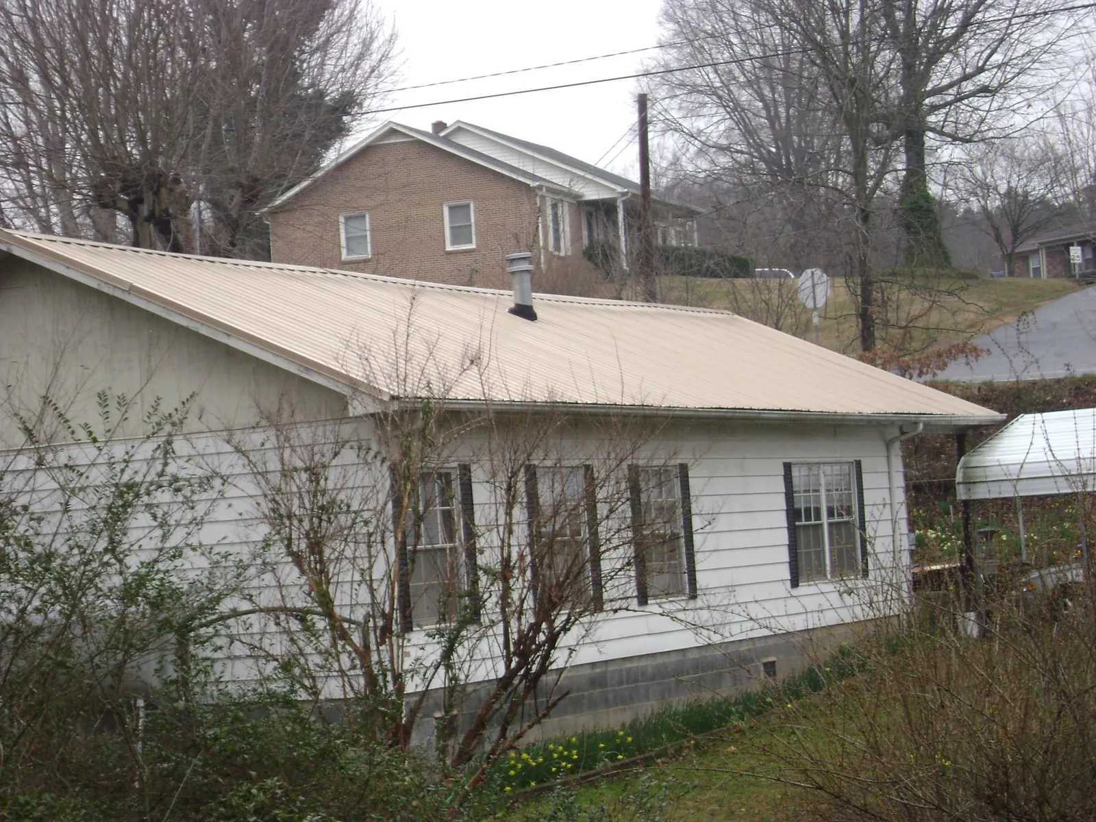 Tan metal roof on a white sided house set into a hillside — Commercial Roofing by Roofing Brothers in Montoursville